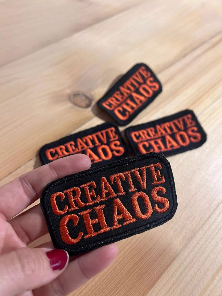 Creative Chaos embroidered iron-on patch with coral-red lettering on a black background