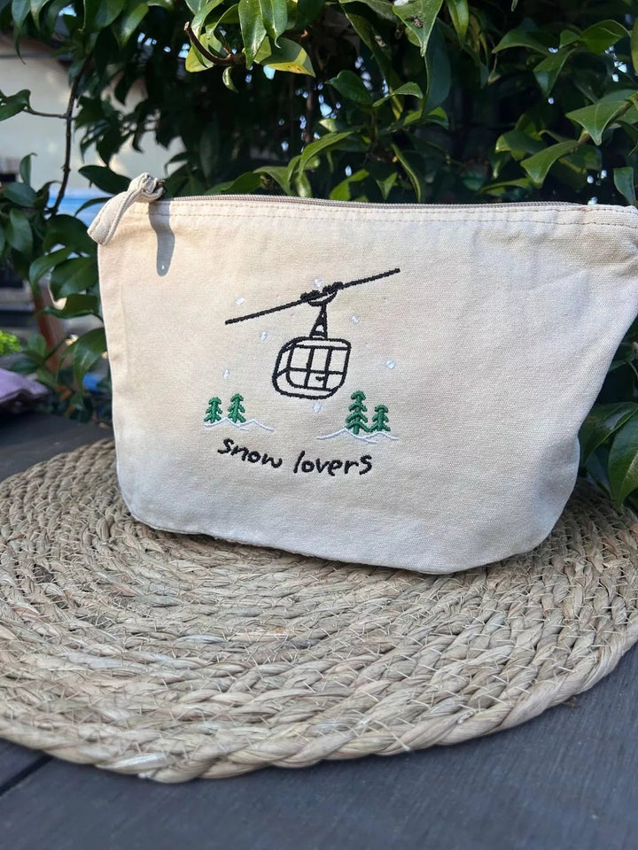 washed beige faded cotton travel pouch with embroidered cable car, pine trees, snow and Snow Lovers lettering