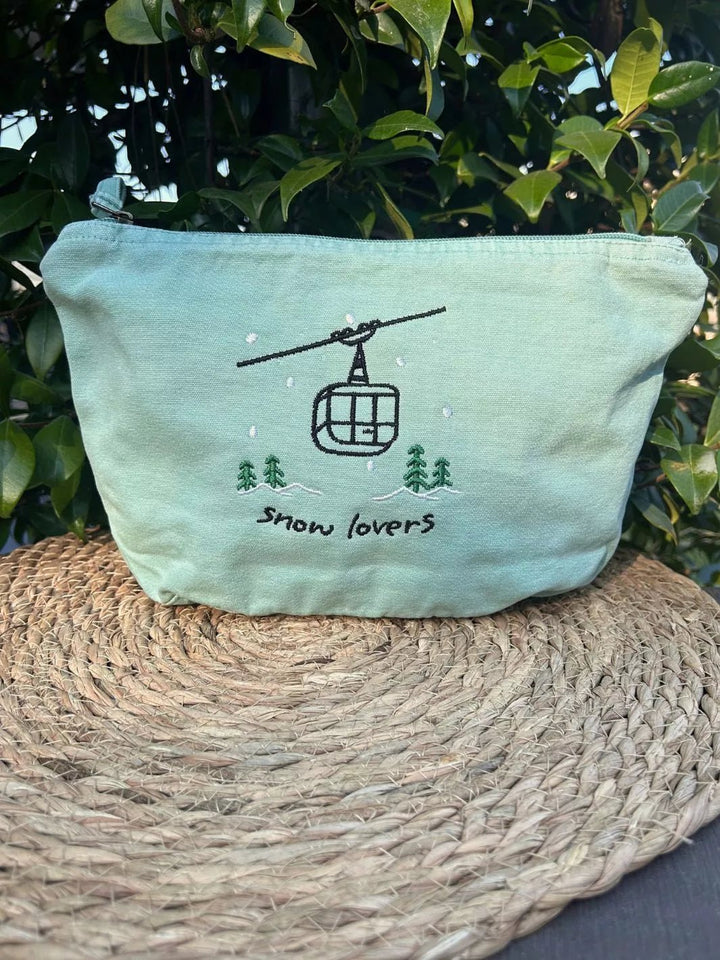 washed sage faded cotton travel pouch with embroidered cable car, pine trees, snow and Snow Lovers lettering