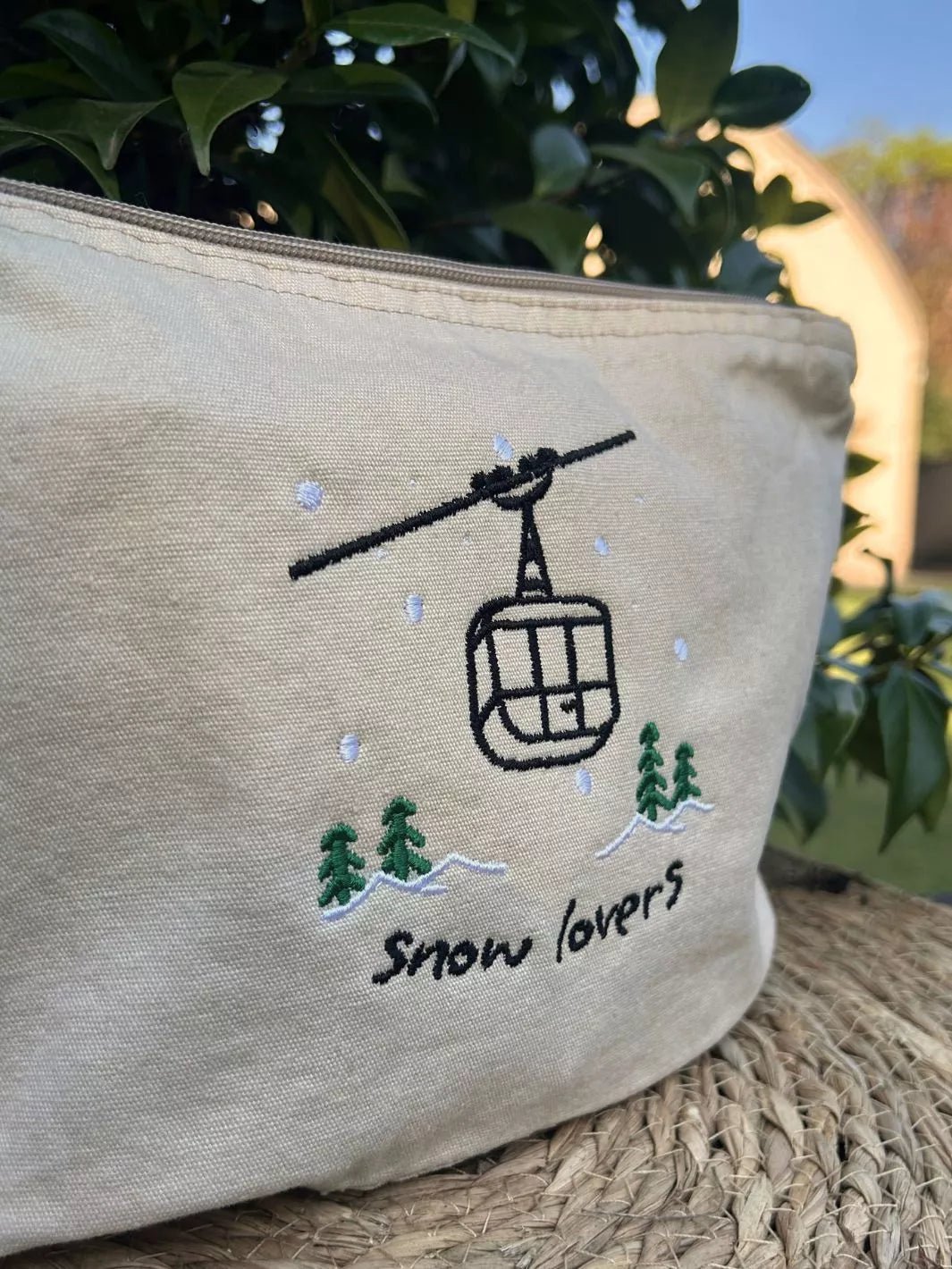 washed beige faded cotton travel pouch with embroidered cable car, pine trees, snow and Snow Lovers lettering