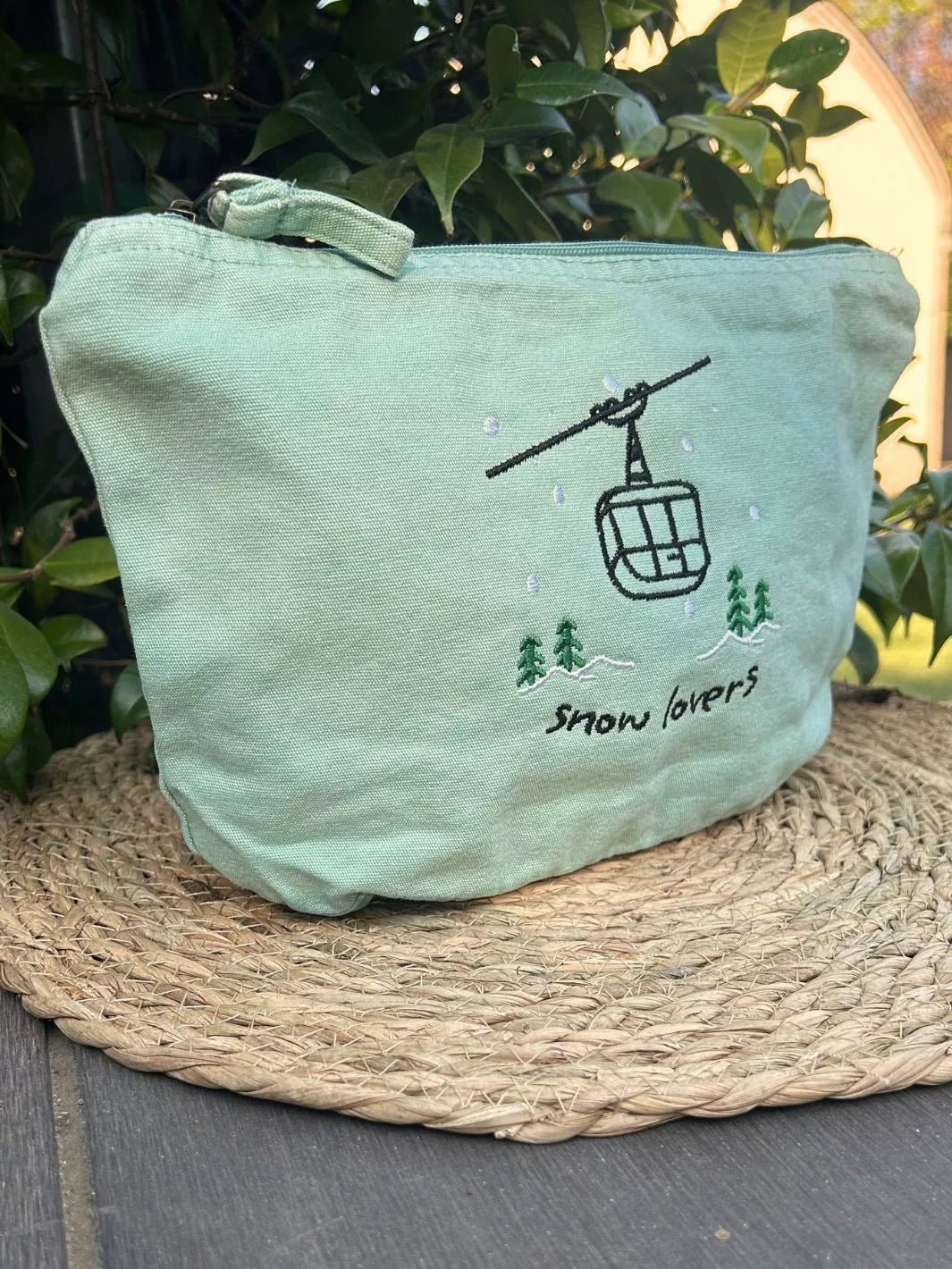washed sage faded cotton travel pouch with embroidered cable car, pine trees, snow and Snow Lovers lettering