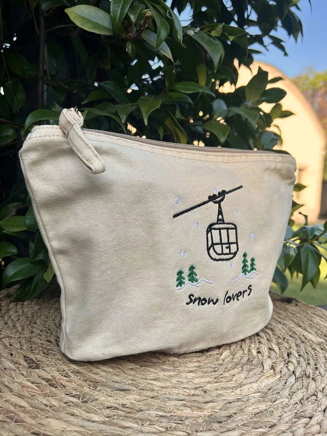 washed beige faded cotton travel pouch with embroidered cable car, pine trees, snow and Snow Lovers lettering