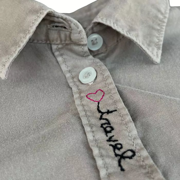 women's shirt in washed beige organic cotton with airplane embroidery and the words "travel" with heart and "explore"