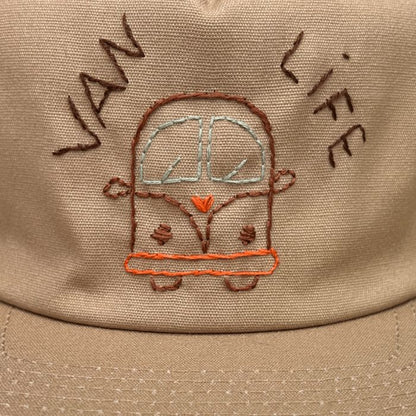 Sand-colored snapback with a camper and the words "van life" embroidered on it